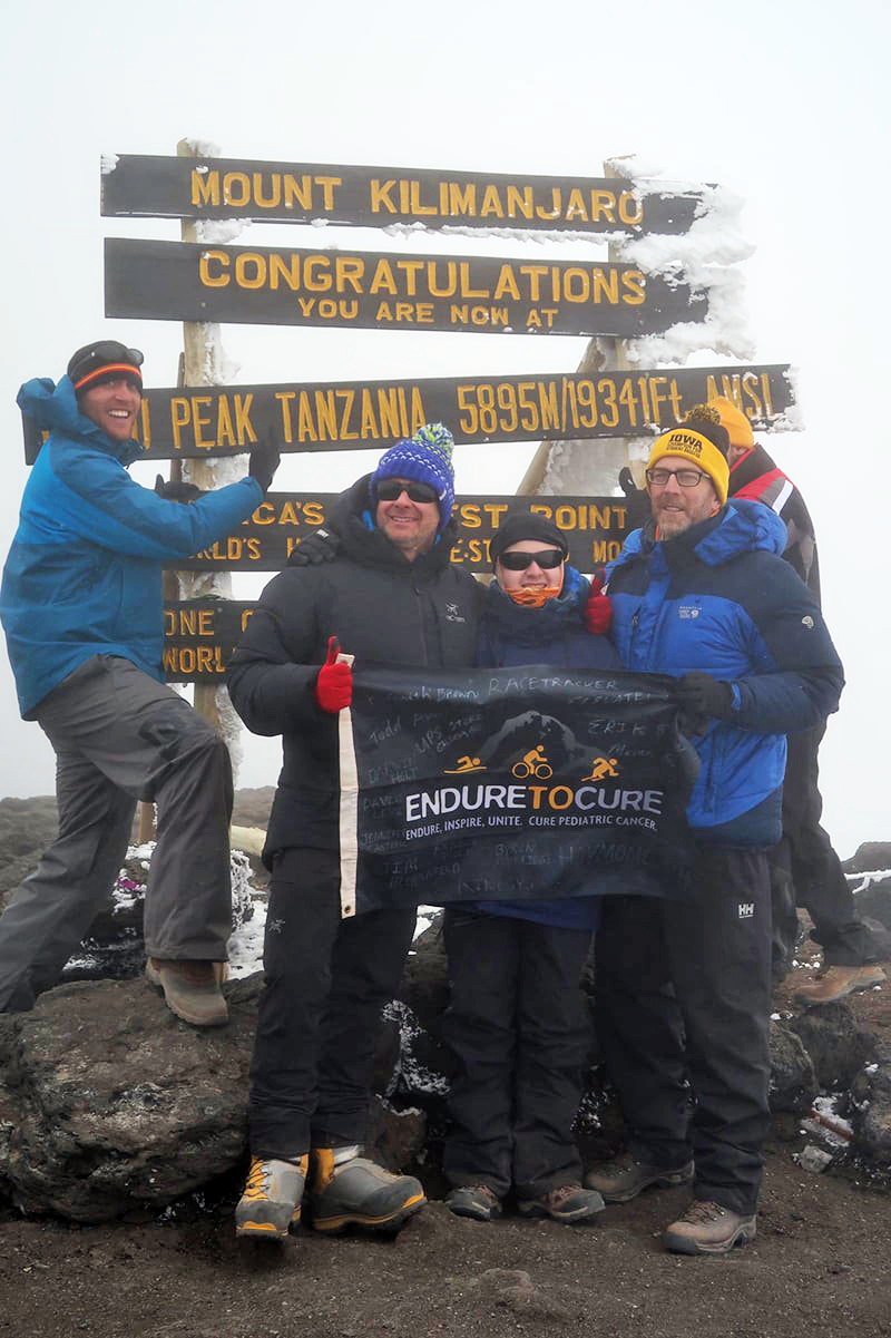 Nick Claudio and Jason Sissel holding an "Endure to Cure" Banner with other hikers at the summit.