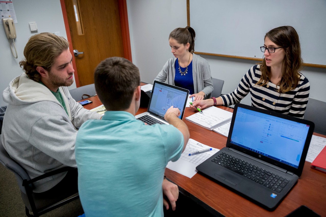 4 students meeting with laptops in a conference room
