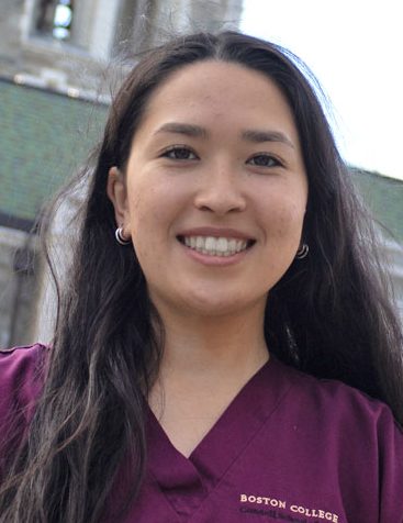 May Tadano in maroon scrubs in front of BC's Gasson Hall