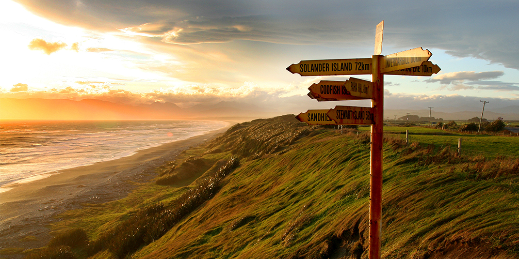 SIGNPOSTS NEXT TO A CLIFF AND OCEAN AT SUNSET