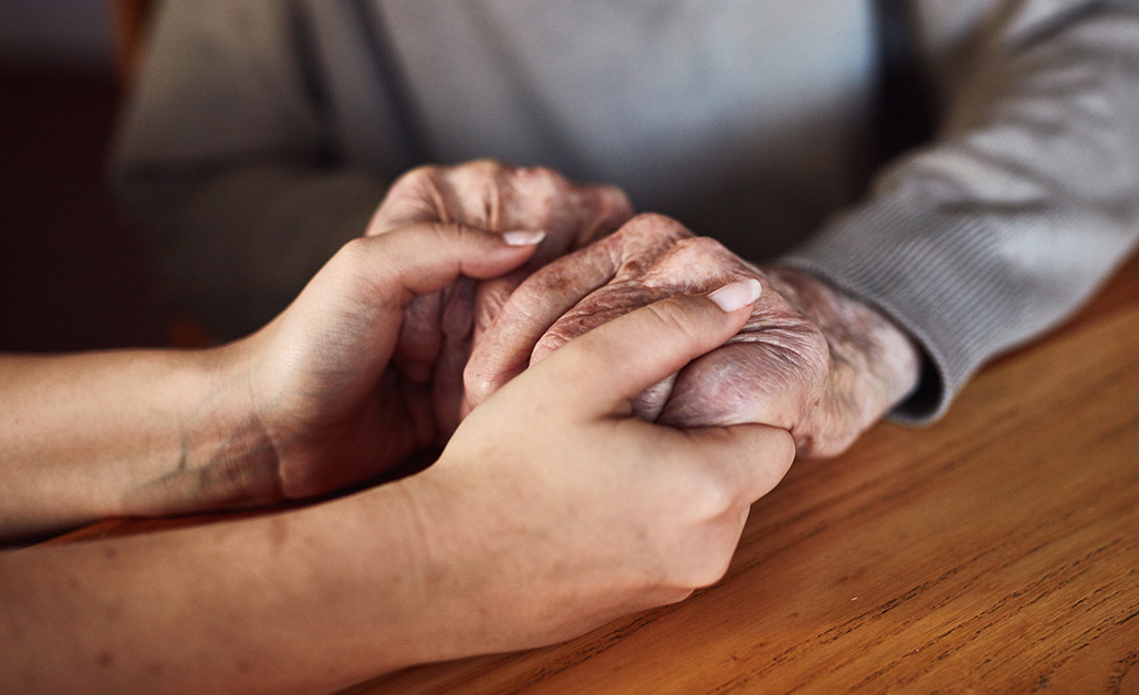 A friend holds the hand of an older adult to offer support 