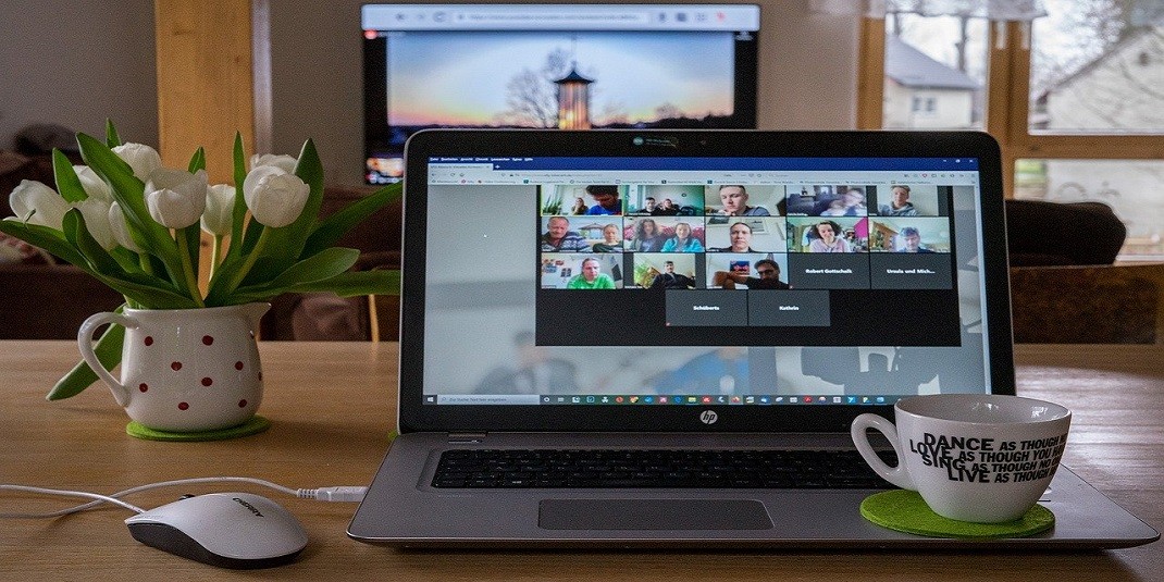 a laptop with a mug and a vase of flowers at a table