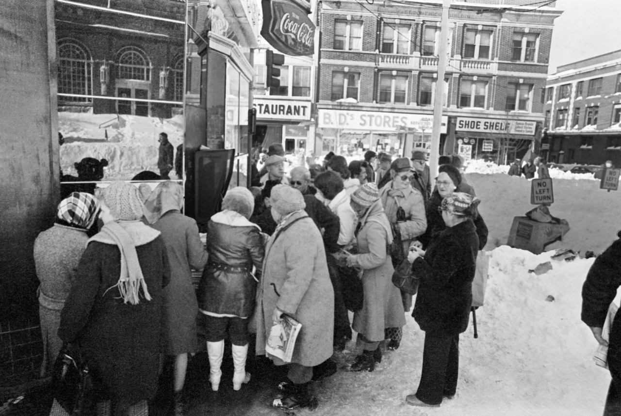 Black and white photo of people gathered at a newsstand