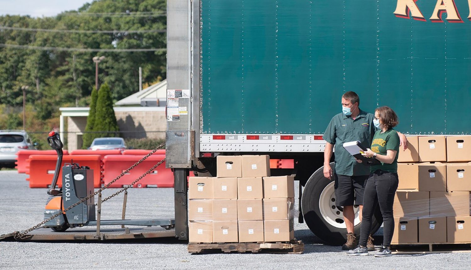 Two people standing next to a truck and piles of boxes
