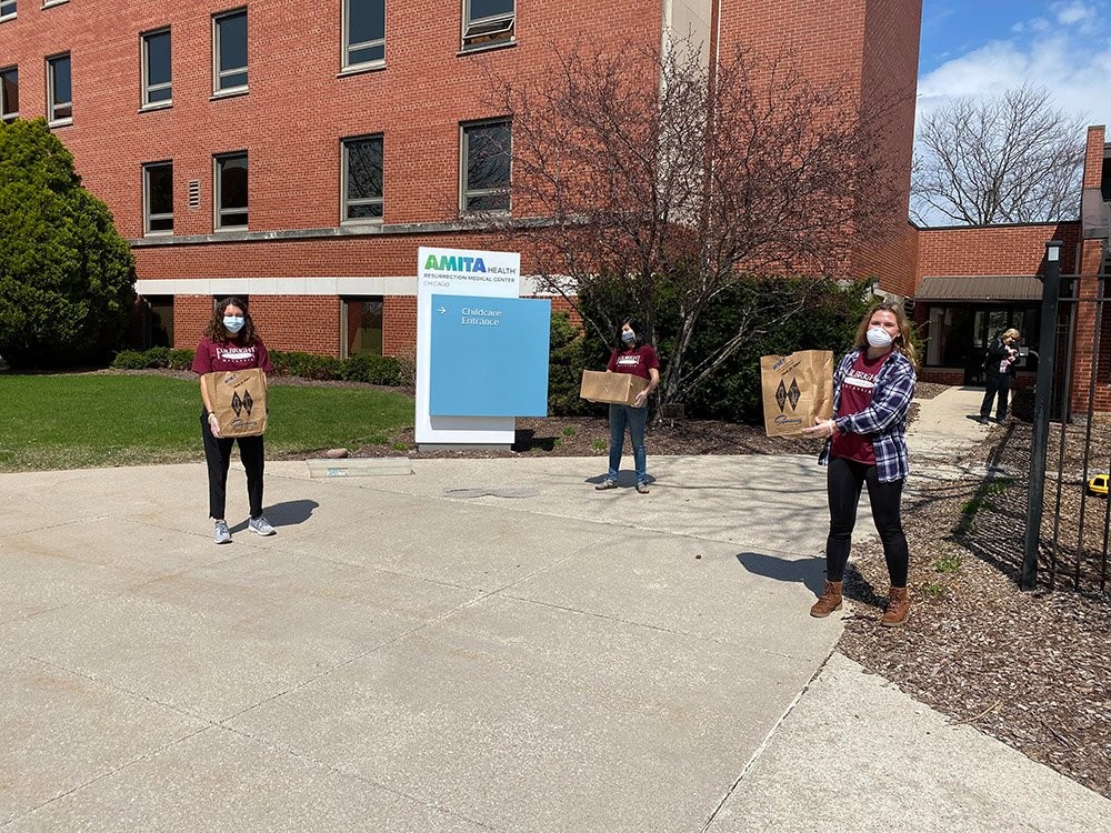 The three founders of Feed the Front Lines Chicago, standing 6 feet apart holding paper bags