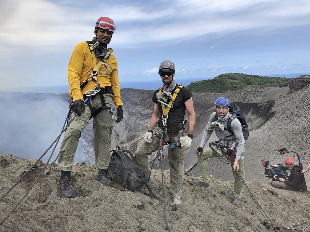 Will Smith, Jeff Johnson, and Erik Weihenmayer wearing climbing gear standing at the rim of Mount Yasur.