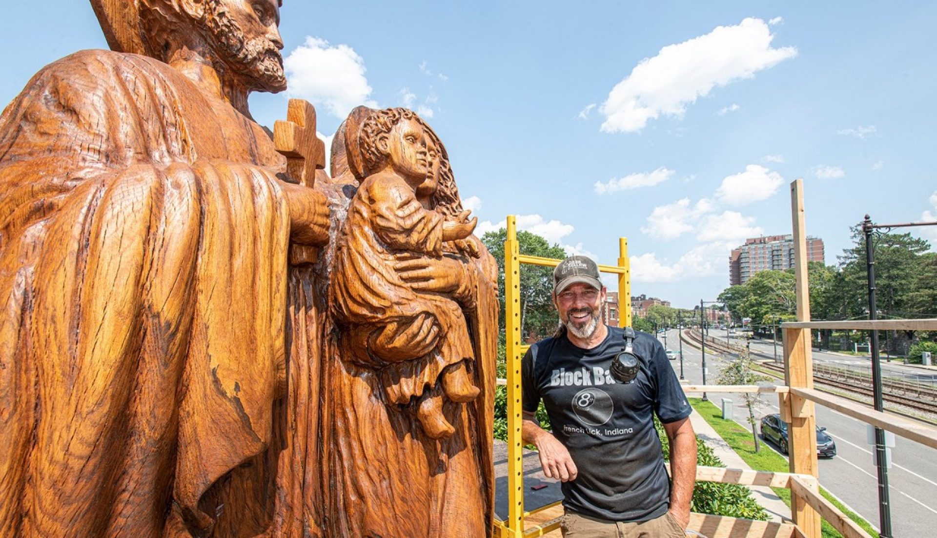 A man standing next to a large wood sculpture