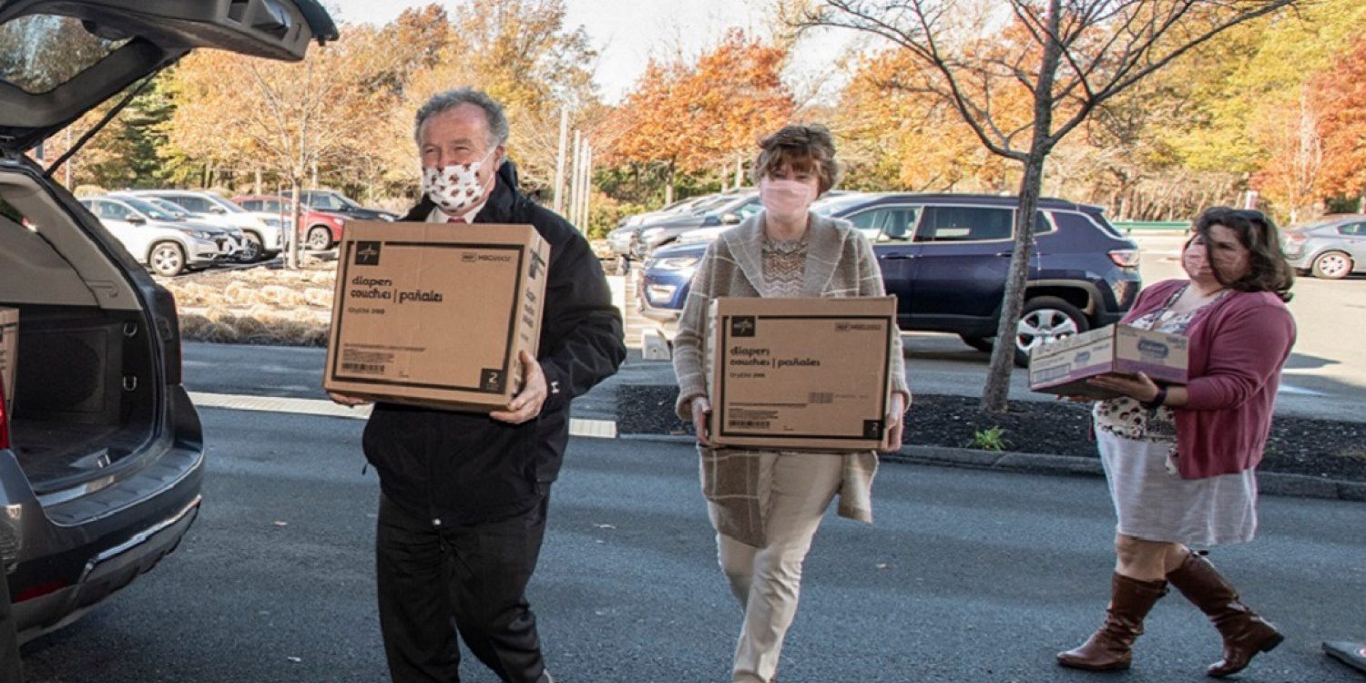Three people carry boxes to a car