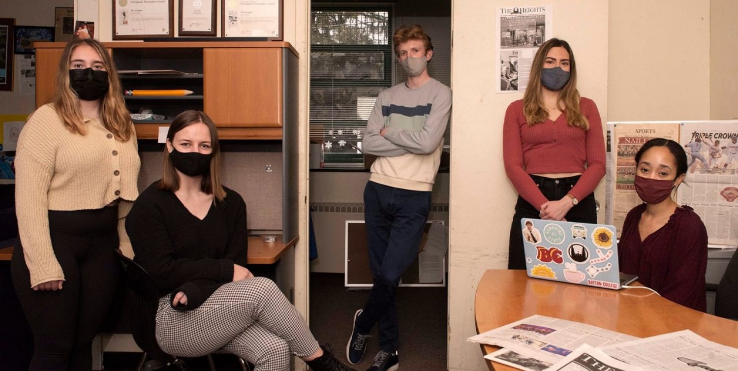 Five students wearing masks seated in a news room