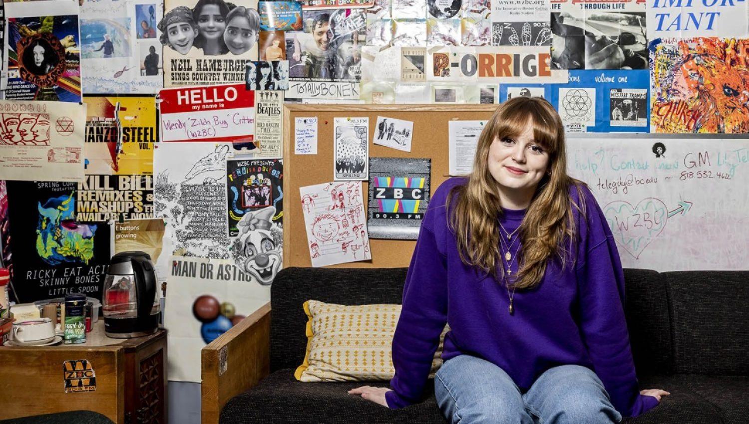 Lily Telegdy sitting on a couch against a wall of posters and stickers