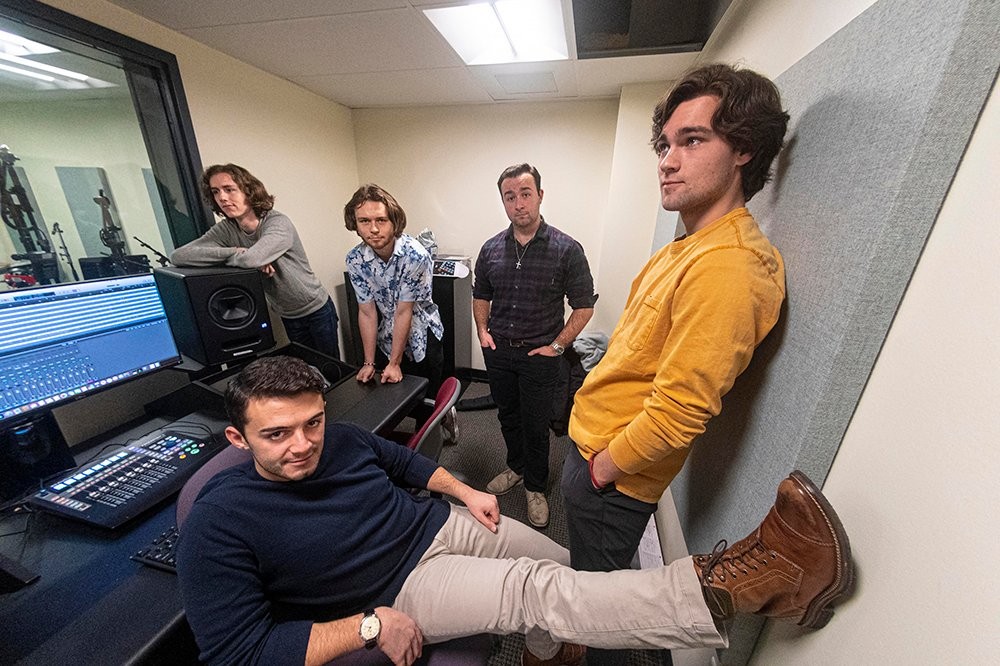 Five members of a band standing in a recording studio