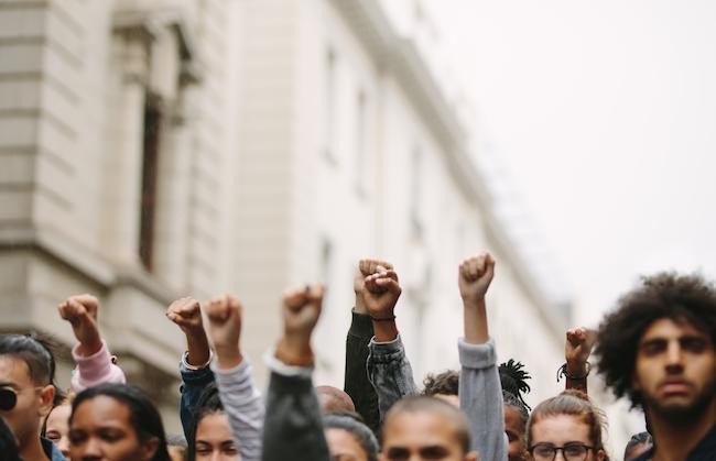 photo of various people outside a building, some raising their hands