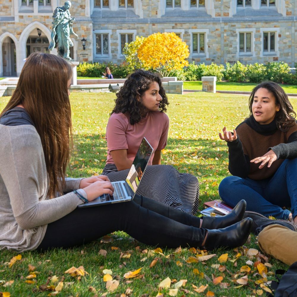 Three young women sitting on the grass in discussion