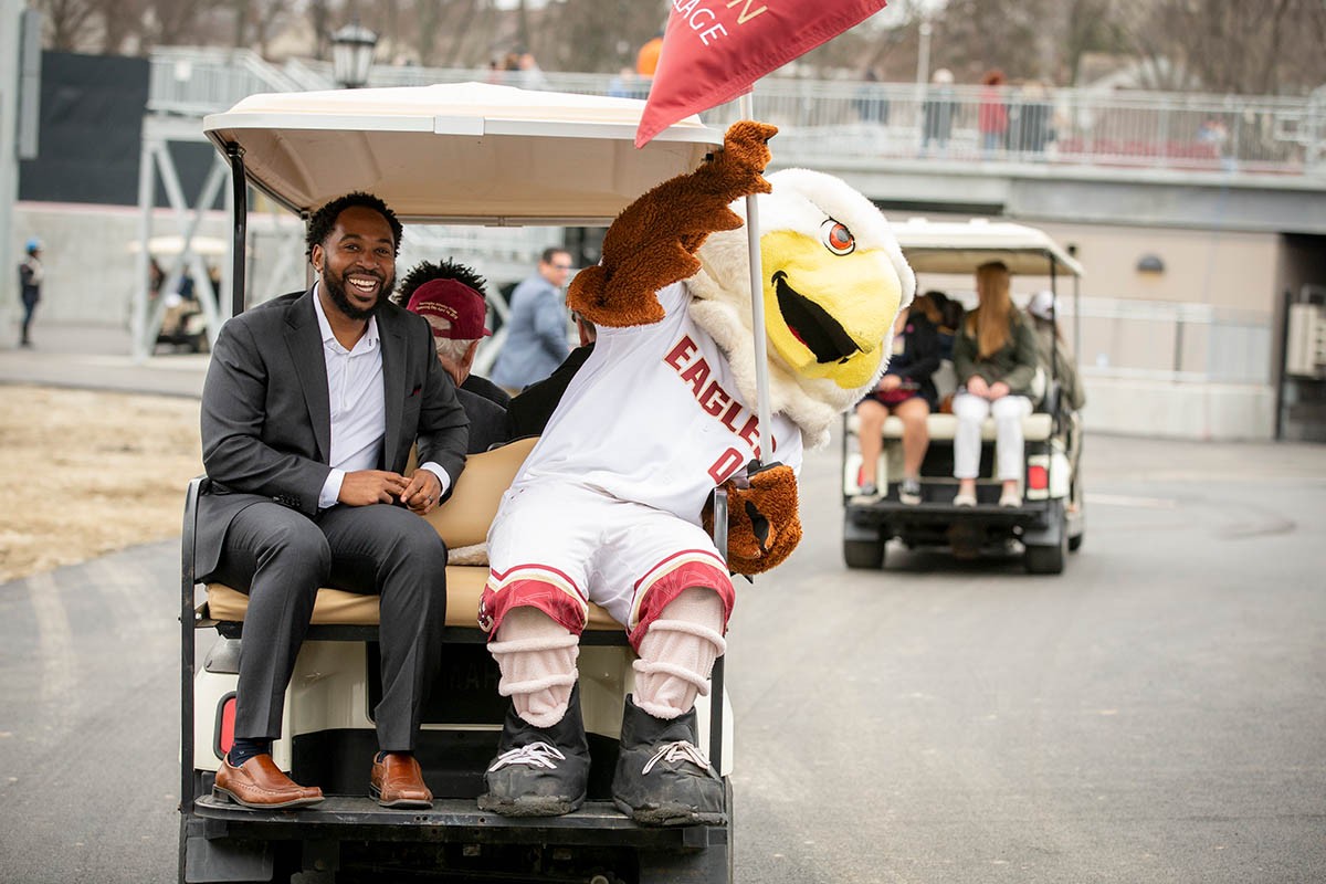 Martin Jarmond rides a golf cart with BC Eagles mascot. 