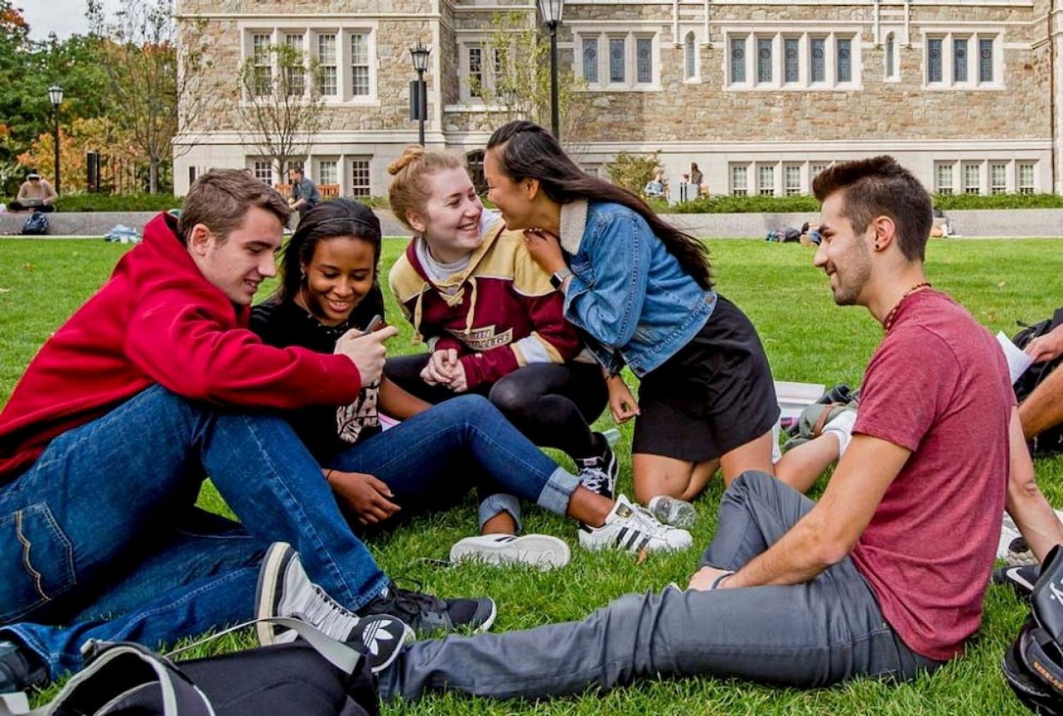 group of boston college students sitting and talking on the grass