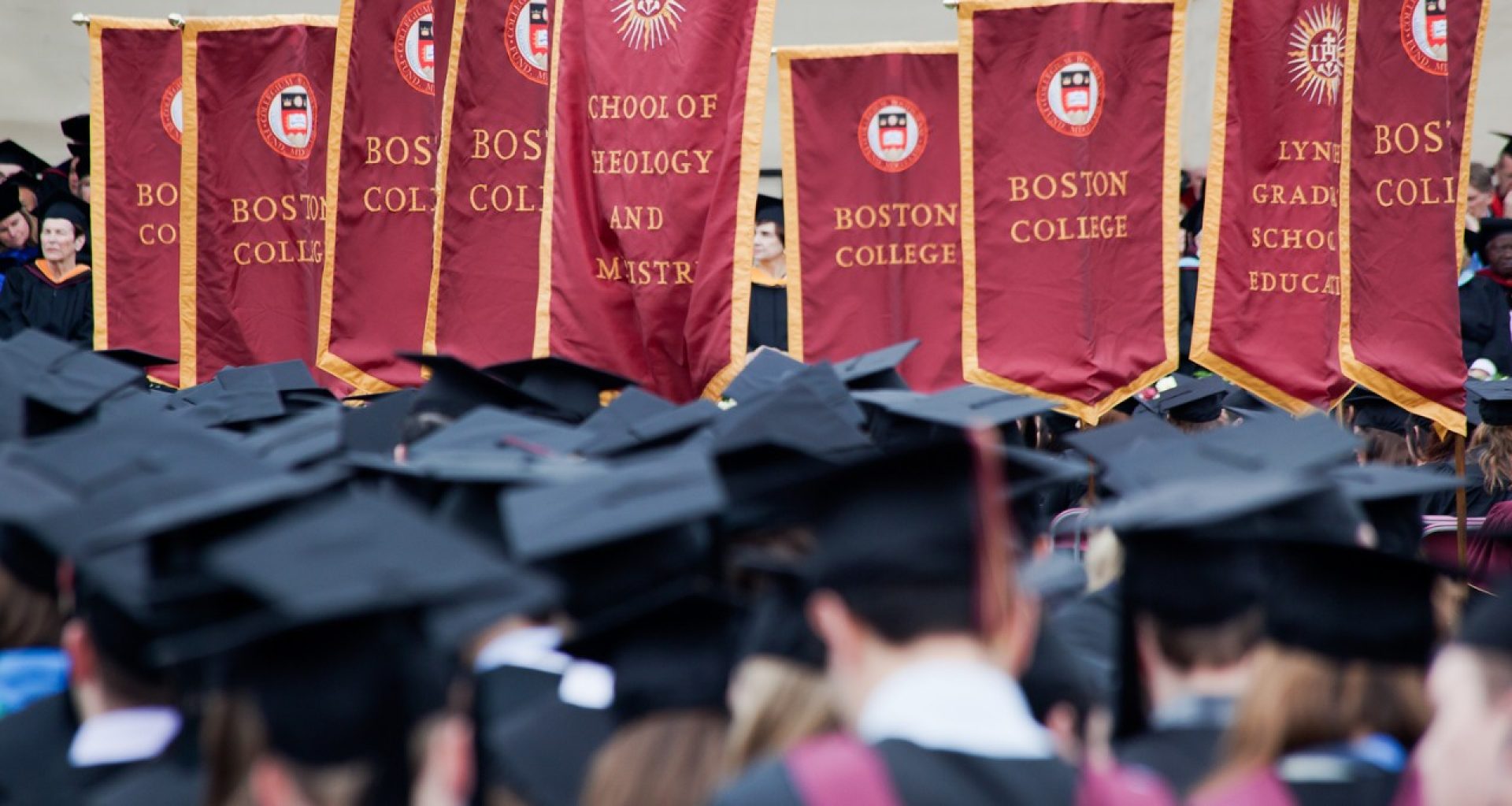 graduates at Commencement standing in front of Boston College maroon and gold banners