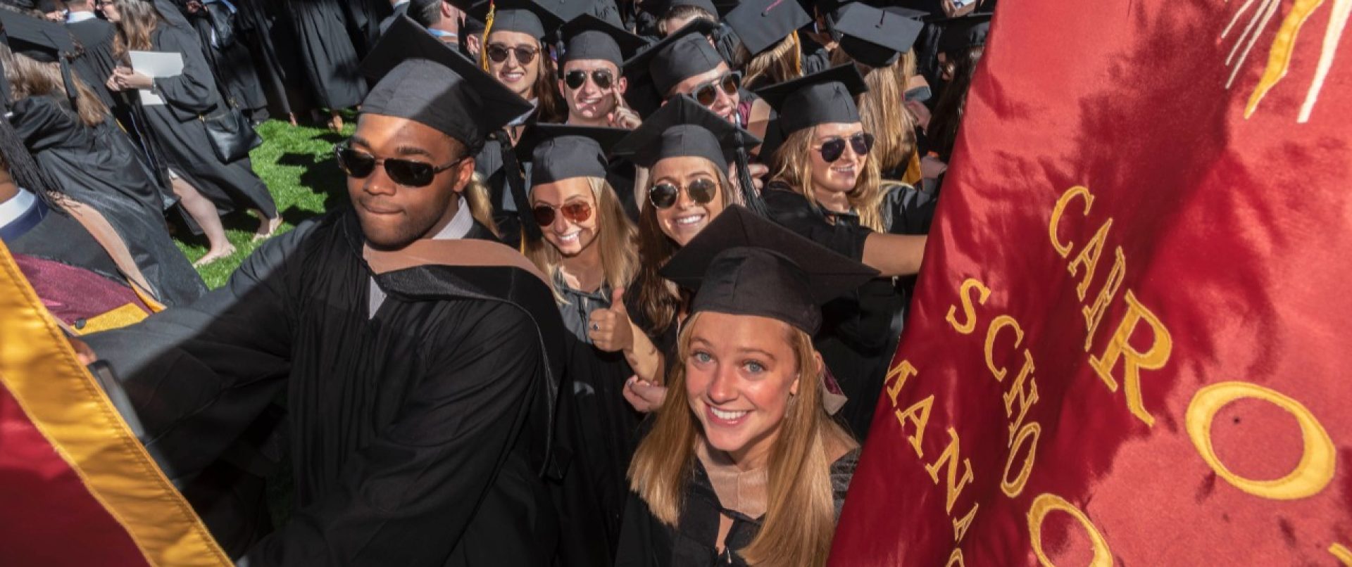 graduates at Commencement standing in front of Boston College maroon and gold banners