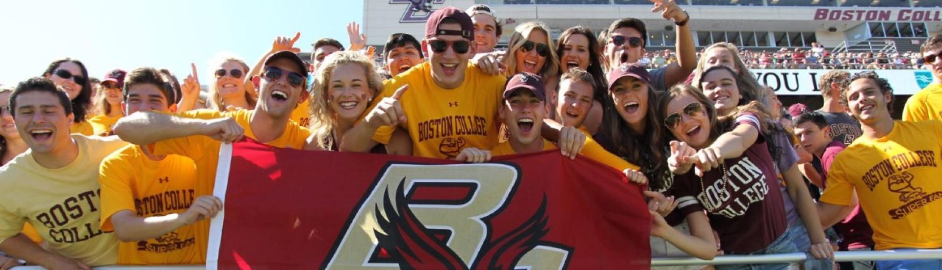 students cheering and holding a BC banner at a football game