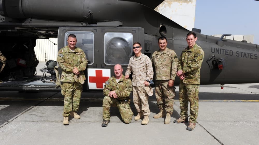 5 men in Army uniforms in front of a helicopter