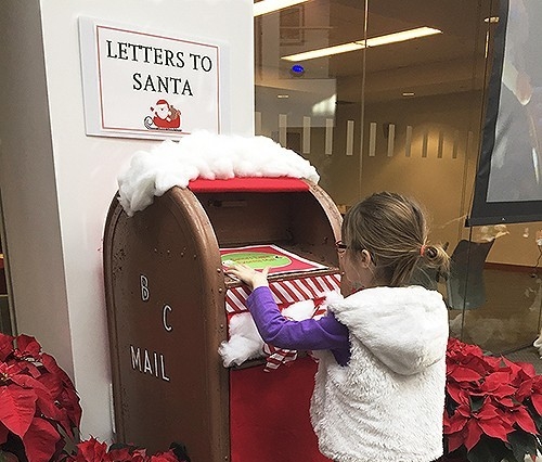 a young girl putting a letter to santa in a cardboard mailbox