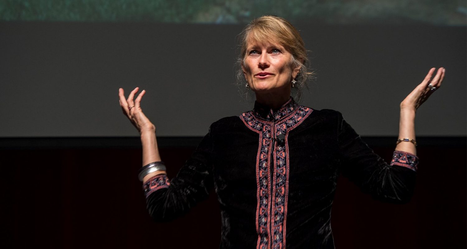 Jacqueline Novogratz standing on a stage, smiling with her hands clasped during a presentation