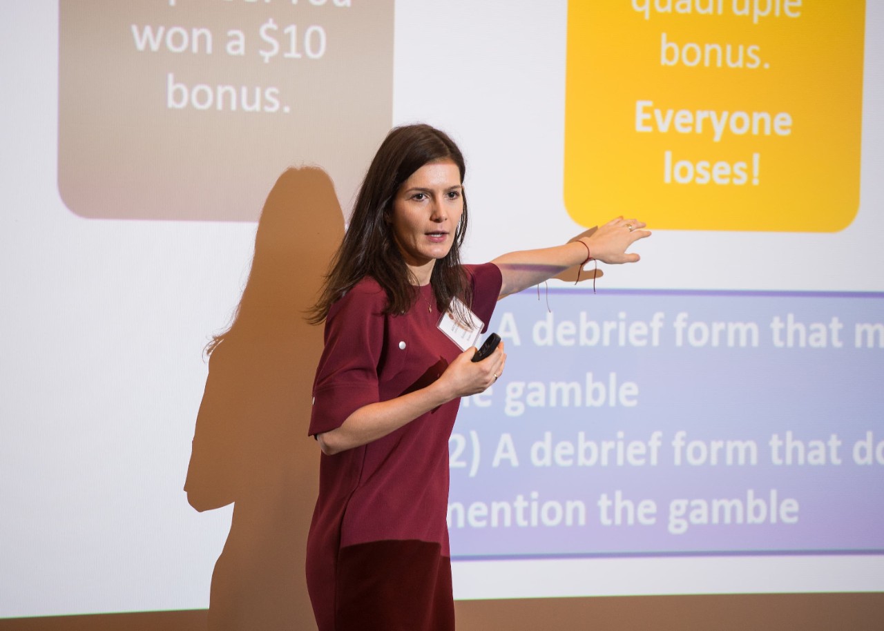 Hristina Nikolova presenting in front of a projection on a screen. She is pointing to a text box on the screen