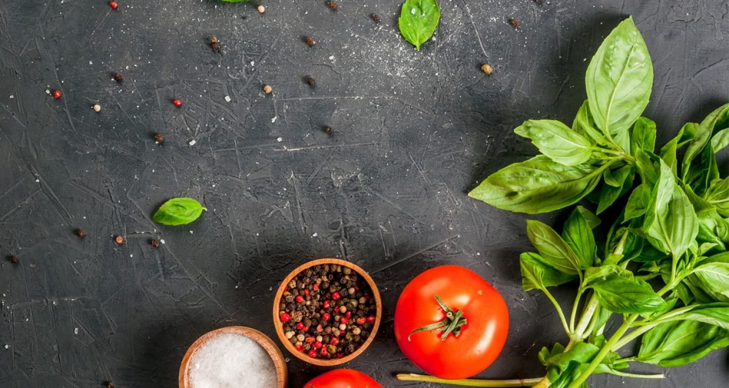 overhead shot of tomatoes, basil, and bowls of spices on a counter