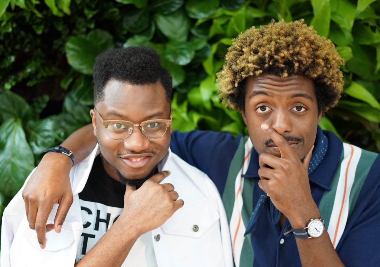 Ivan Alo and LaDante McMillon posing with their arms around each other in front of a green leafy background