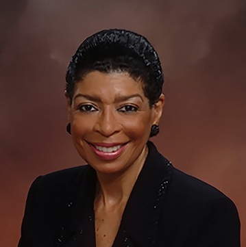 Headshot of smiling Black woman in blazer, short hair and black earrings.