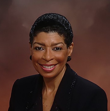 Headshot of smiling Black woman in blazer, short hair and black earrings.