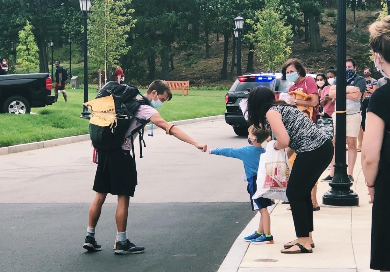 Gordon Wayne, wearing his backpack with its "end homelessness" sign, fist bumps a masked child outside alumni stadium