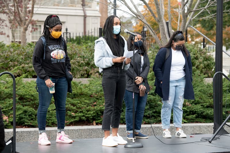 two black women stand behind a table of wigs with textured hair