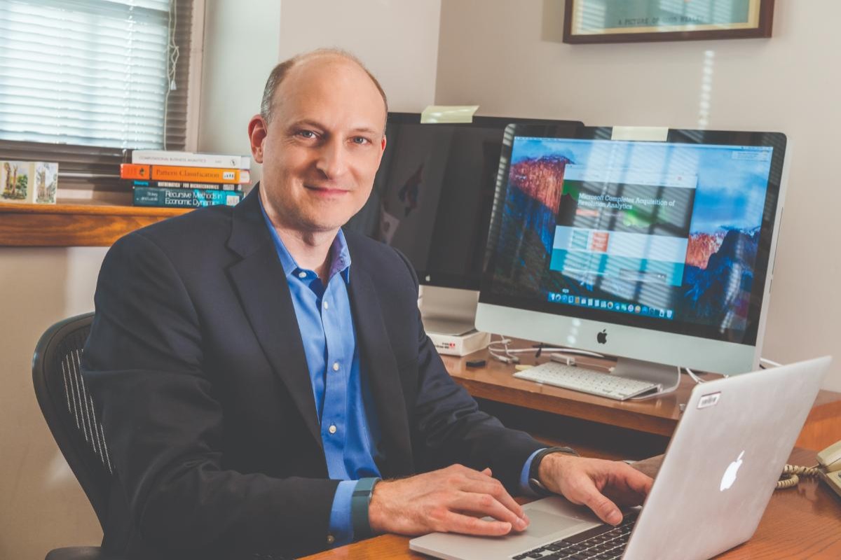 Smiling man in suit jacket at a desk with hands on laptop