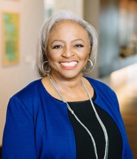 African American woman smiling, in black blouse and blue cardigan