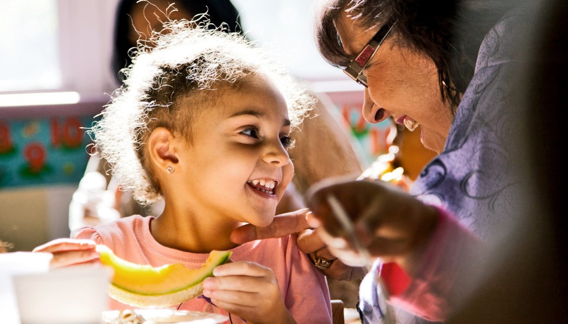 A young black girl smiles at an older black woman, United Way logo is in the lower right corner