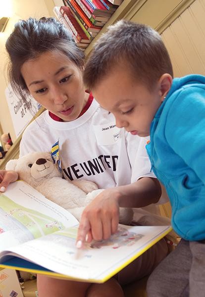 an asian woman in a United Way tshirt reads to a child