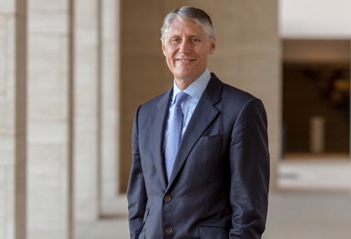 White man of middle age in a busines suit, standing in a corridor.