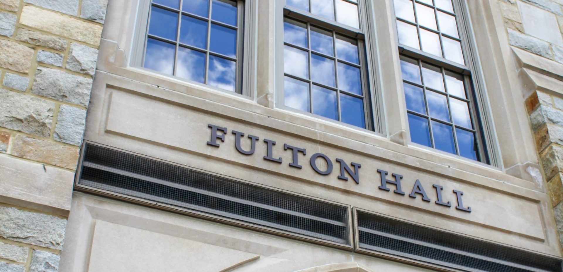 Fulton Hall entryway with blue skies reflected in the window