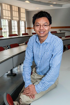 Professor Zhuoxin (Allen) Li in button-up shirt, sitting on edge of table