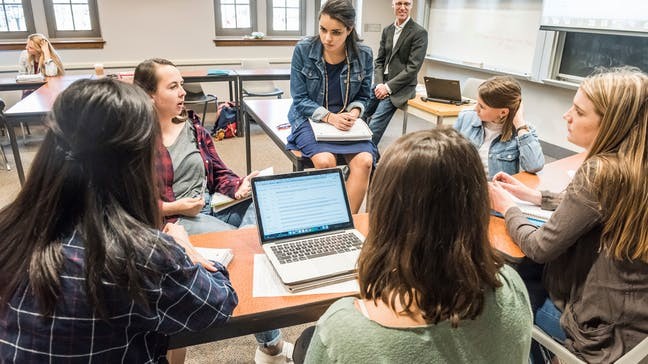 Photo of Students having a discussion, sitting around a laptop in a classroom