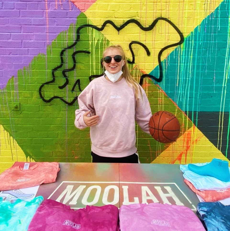 Photo of Natalie White in front of a brightly colored mural holding a basketball