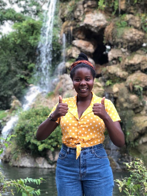 Liliane standing in front of a waterfall giving two thumbs up