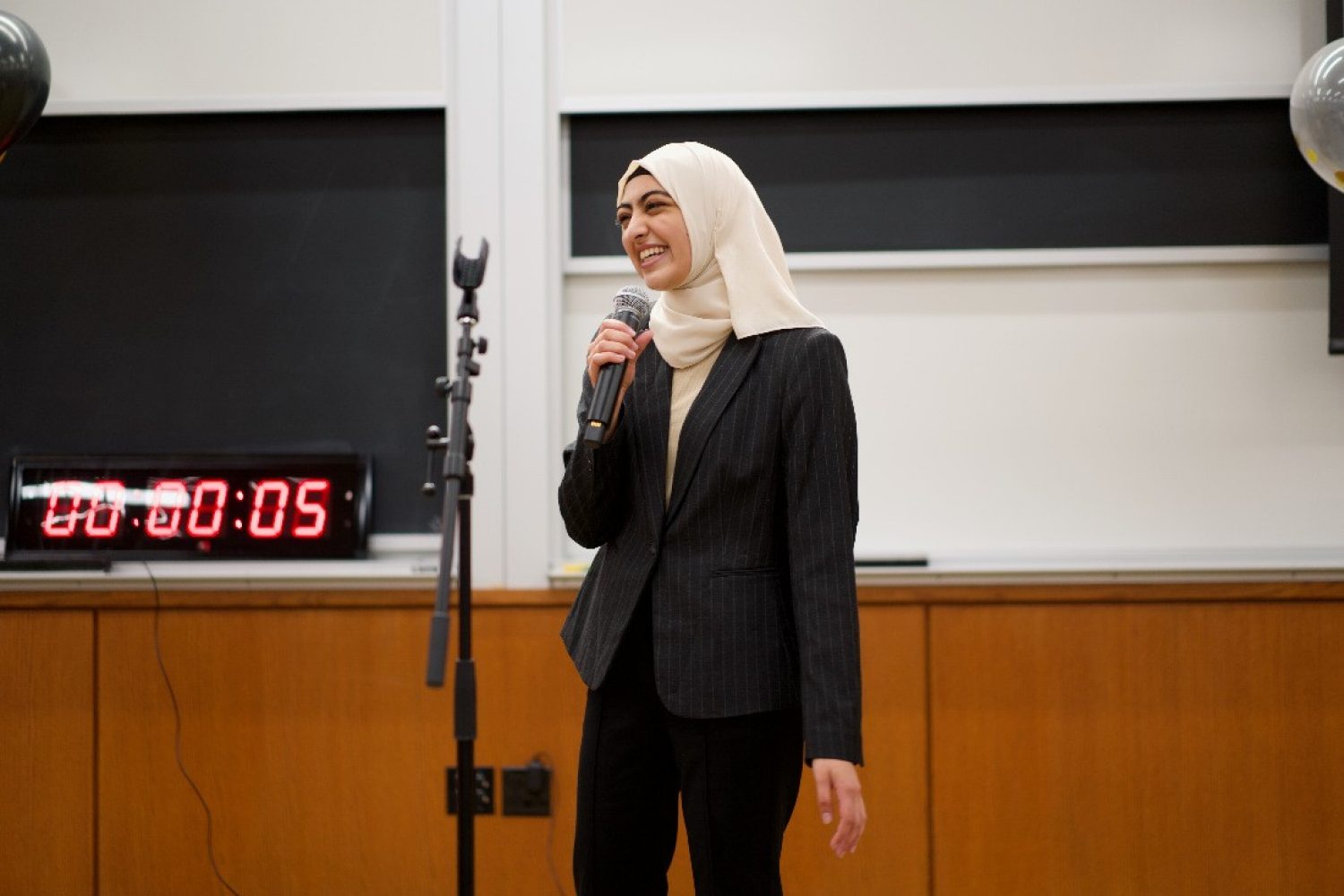 A photo of Zarah Lakahni presenting at the 2022 Elevator Pitch competition. She is smiling at the judges while she speaks into a microphone, with only five seconds left on the clock.