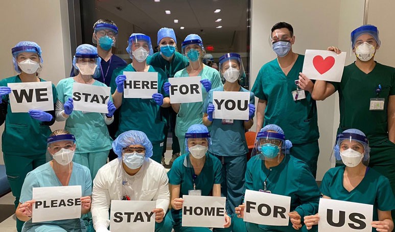 Night-shift nurses at NYU Langone hold signs that say "We stay here for you, please stay home for us."