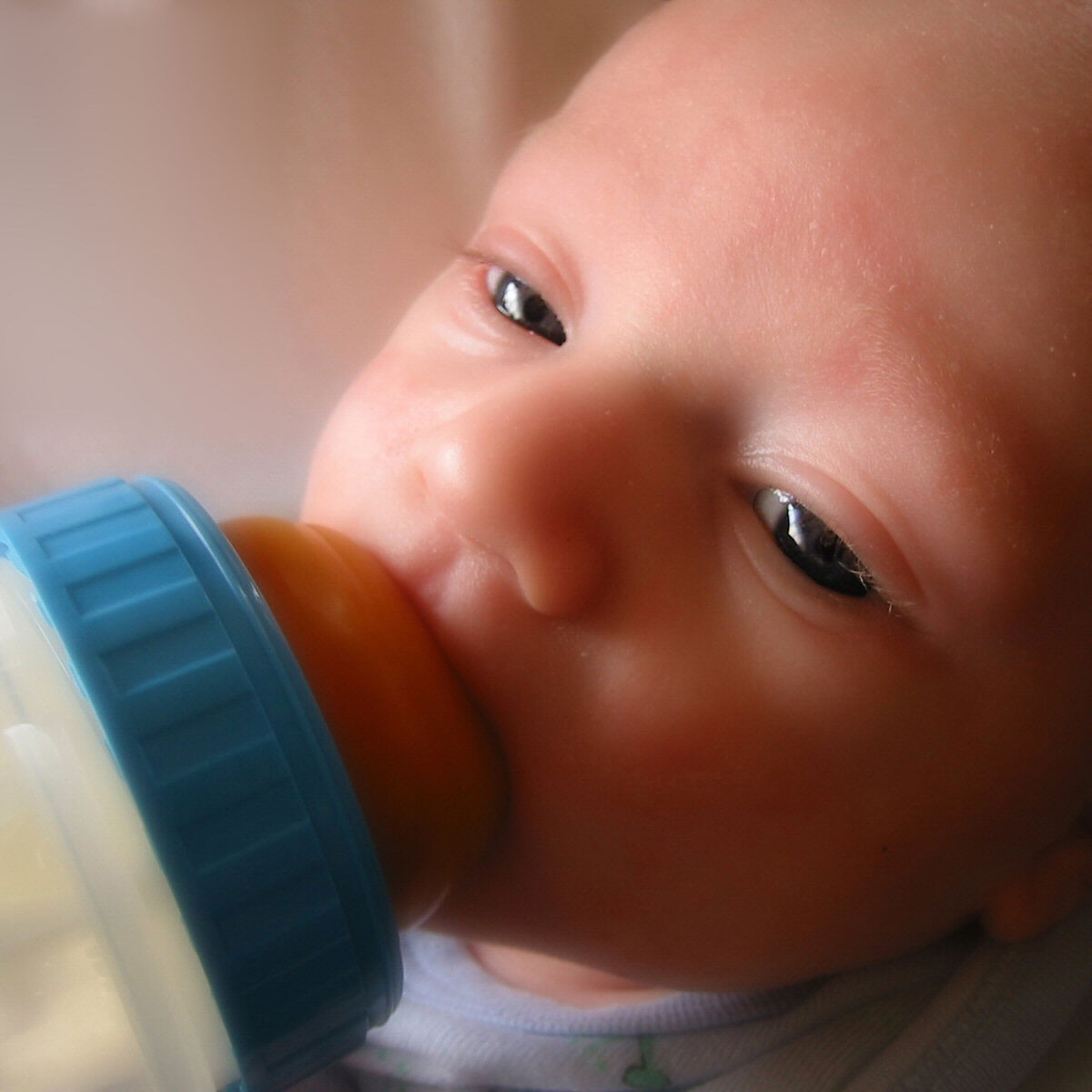 Baby feeding from a clear bottle with a blue top and tan nipple