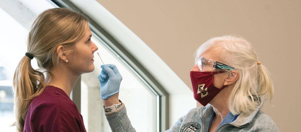 Colleen Simonelli (on right in a mask) swabs the nose of a CSON undergrad in scrubs