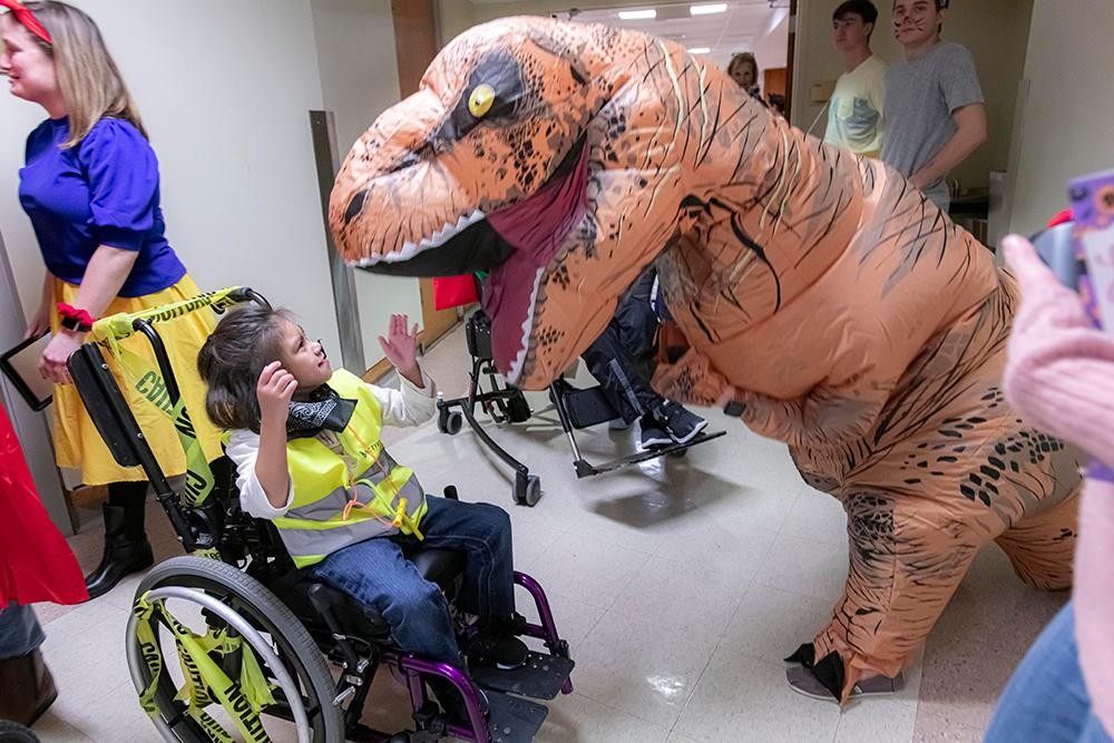 A student in a wheelchair next to a person dressed up as a dinosaur