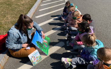 A teacher and children sitting on the grouund reading a book