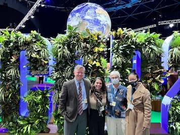 Photo of Image of people posing in front of plants and a statue of Earth