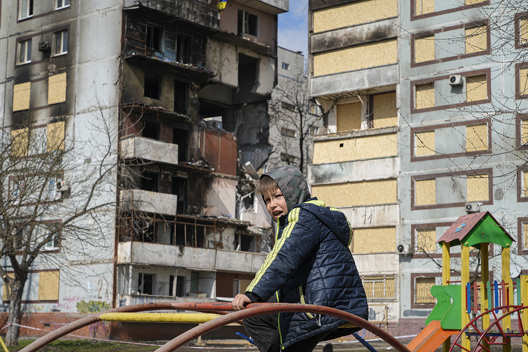 A boy sits on a climbing frame in a playground in front of missile-damaged buildings ahead of a visit by Ukraine's President Volodymyr Zelenskyy in Zaporizhzhia, Ukraine, Monday, March 27, 2023. Zelenskyy has been increasing his travel across Ukraine as his country's war with Russia enters its second year. A team of journalists from The Associated Press traveled with Zelenskyy aboard his train for two nights as he visited troops along the front lines and communities that have been liberated from Russian control. (AP Photo/Efrem Lukatsky)